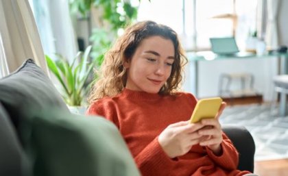 Woman looking at a smart phone while sitting on a lounge.